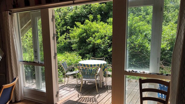 A sliding glass door leading to an outdoor deck with a table and chairs, surrounded by greenery.
