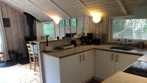 A kitchen with wooden cabinets, a stove, a sink, and a window with a view of trees.