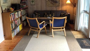 A cozy room with a wooden ceiling, a bookshelf, a sofa with sunflowers, and a dining area with chairs.