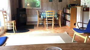 A cozy cabin interior with a wooden table, chairs, a bookshelf, and a fireplace.