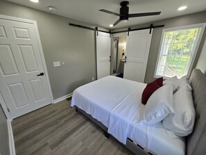 A bedroom with a bed, a ceiling fan, a window with blinds, and a door. - Silver Group Rentals Presents The Silver Spot (Atlanta)