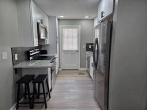 A modern kitchen with a microwave, oven, and refrigerator. There are two bar stools and a window with blinds. - Silver Group Rentals Presents The Silver Spot (Atlanta)
