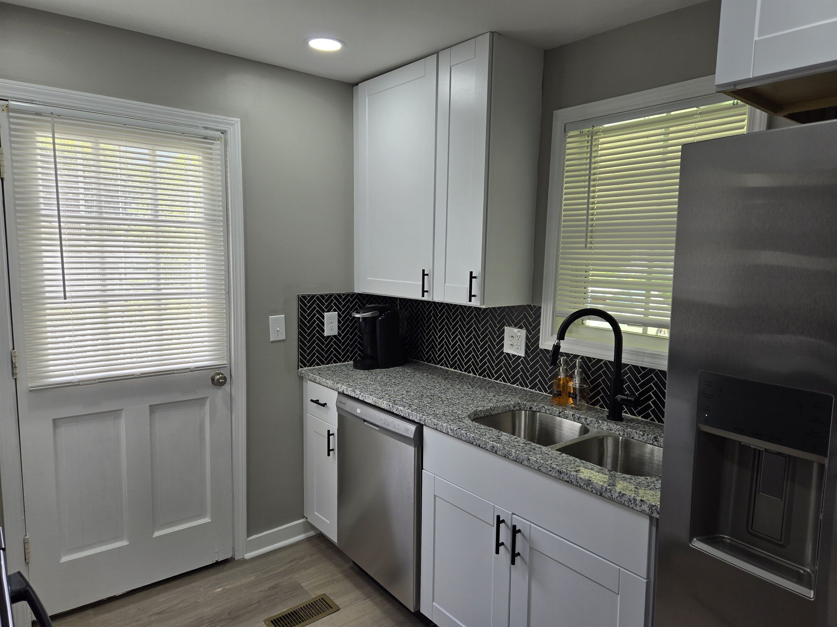 A kitchen with white cabinets, a granite countertop, a stainless steel sink, and a built-in dishwasher.