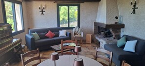 Un salon chaleureux avec une cheminée, un piano et un coin repas comprenant une table et des chaises.