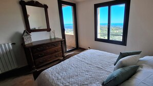 Un dormitorio con cama, cómoda, espejo y vista al mar a través de una ventana.