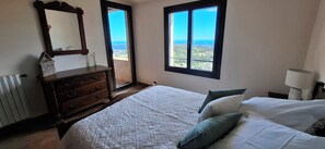 Une chambre Ă coucher avec un lit, une commode, un miroir et une vue sur la mer par la fenĂȘtre.