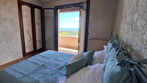 Un dormitorio con cama, almohadas, cabecera de madera, ventana con vista y puerta que da a un balcón exterior.
