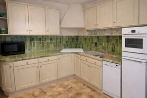 Une cuisine avec des armoires de couleur beige, un dosseret de carrelage vert, un four à micro-ondes, un évier et un four double.