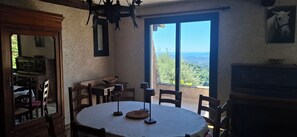 A dining area with a round table, chairs, a chandelier, and a view through large windows. - Provencal house 9 pers, panoramic sea view, pool, jacuzzi, quiet, nature (chateauneuf de grasse)