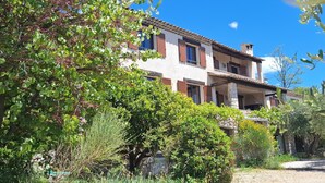 Un edificio de dos pisos con fachada de piedra, varias ventanas con contraventanas y un balcón.