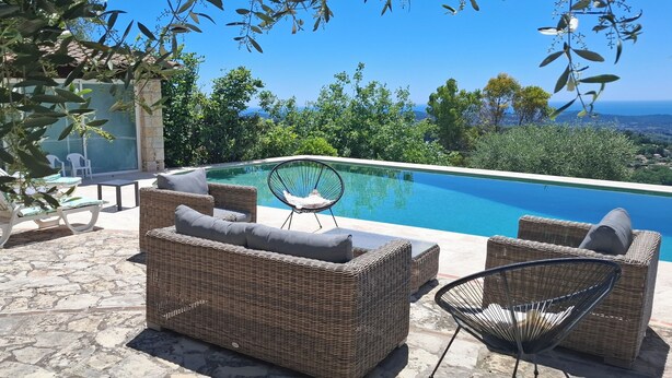 Zona junto a la piscina con mobiliario de mimbre, una estructura de vidrio y vista al océano.