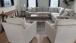 Ein Wohnzimmer mit Ecksofa, zwei Sesseln, einem Couchtisch, einem Fernseher und einer Pflanze.