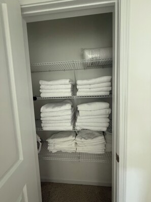A walk-in closet with multiple shelves holding folded white towels. - PSU Kickoff Retreat: Brand New 3 Bedroom Townhome 11 Minutes from Beaver Stadium (Bellefonte)