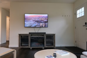 A living room with a flat-screen TV mounted on the wall, a fireplace, a round coffee table, and a door with a window.