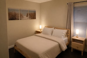 A bedroom with a bed, two bedside tables, a nightstand, and a window with blinds.