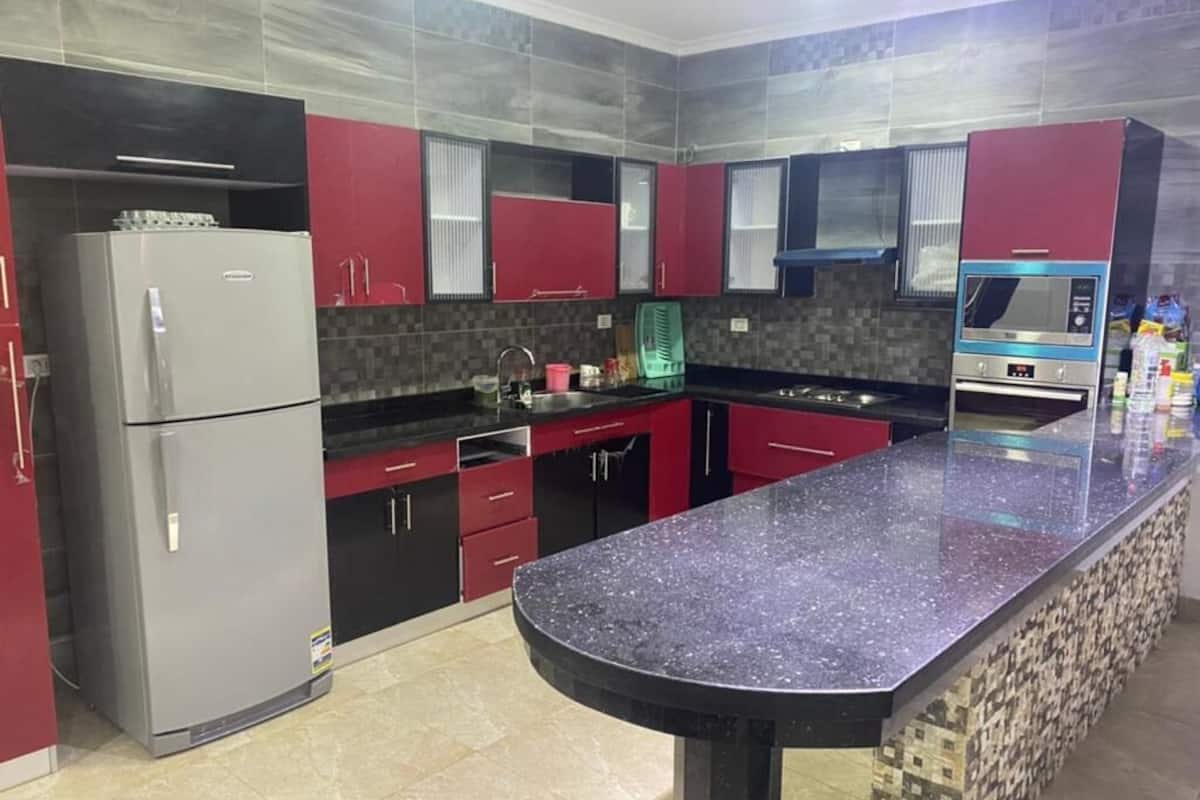 A modern kitchen with red cabinets, a granite countertop, a built-in oven, and a microwave.