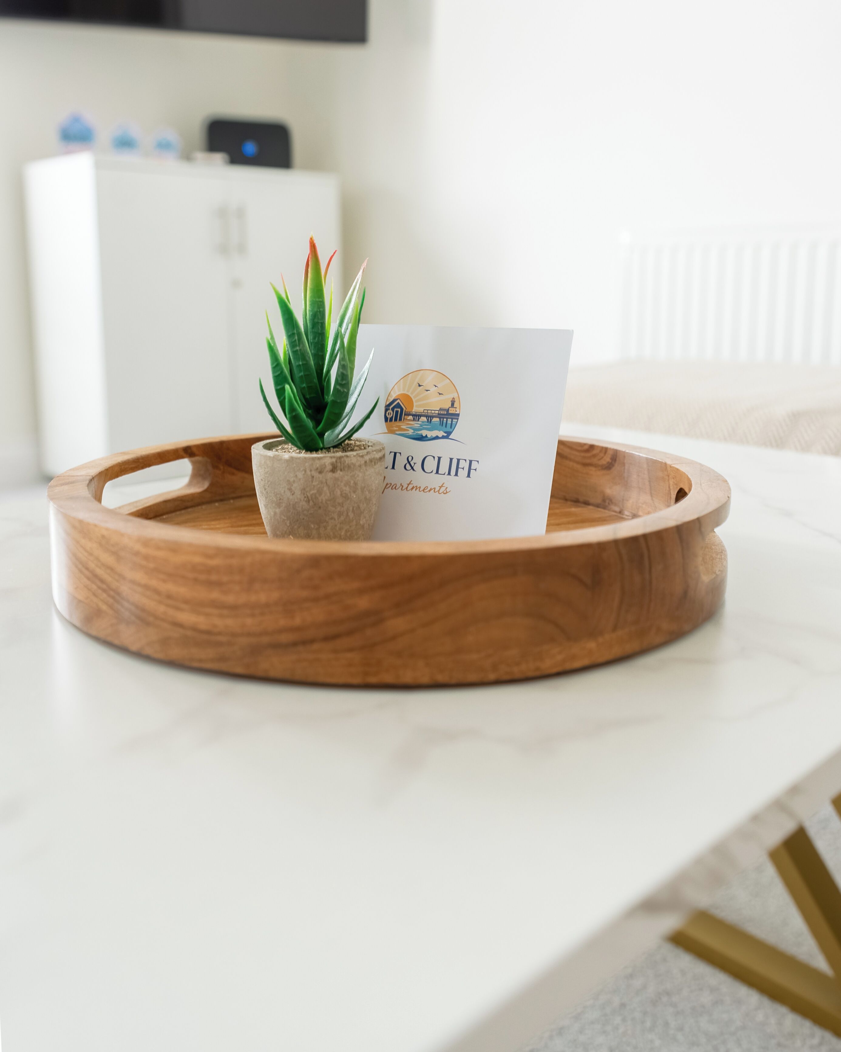 Una bandeja de madera con una planta en maceta y una tarjeta de presentación sobre una superficie blanca.