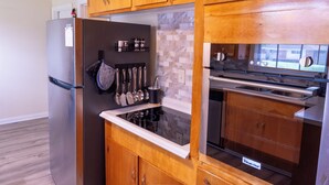 Eine Küche mit Holzausstattung, einem Edelstahlkühlschrank, einem eingebauten Backofen und einer Mikrowelle.