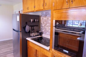 Eine Küche mit Holzausstattung, einem Edelstahlkühlschrank, einem eingebauten Backofen und einer Mikrowelle.