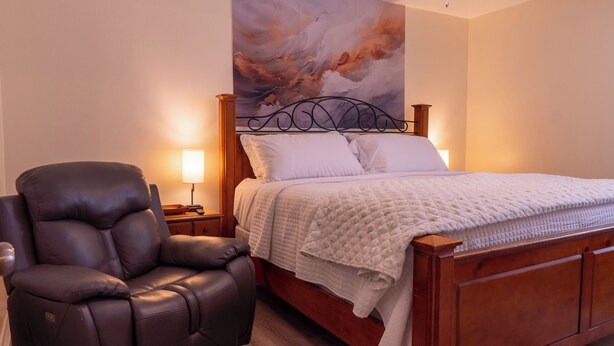 Ein Schlafzimmer mit einem hölzernen Bett, einem Ledersessel, einem Nachttisch und einem Wandbild.