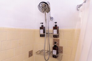A shower with a handheld showerhead, a wall-mounted faucet, and two soap dispensers on a shelf. - 3Bdrm / Game Room Home / World Cup / 15 Min to NRG / 5 Min from Hobby Airport (Houston)