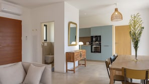 Eine moderne Küche mit Einbauofen, ein Essbereich mit Holztisch und -stühlen sowie ein Badezimmer mit Toilette und Spiegel.