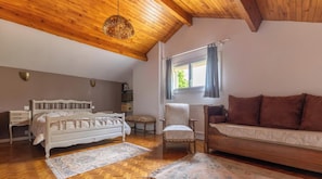 A bedroom with a wooden ceiling, a white bed, a brown sofa, a chair, and a window with curtains. - Les trois chênes - SAYAT (SAYAT)