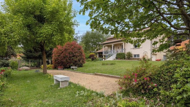 Un jardin avec un banc, un sentier et un bâtiment doté d’un balcon.
