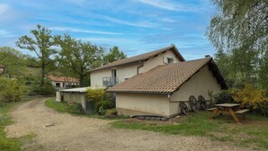 Une maison avec une allée en terre battue, un petit abri de jardin et une table en bois.