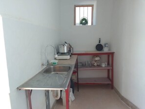 A small kitchen with a sink, a stove, a window, and a shelf with dishes.
