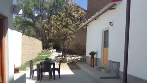 Un patio con una mesa y sillas, una planta en maceta y un muro de piedra.