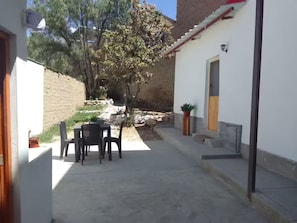 Une cour avec une table et des chaises, un pot de fleurs et un mur en pierre.