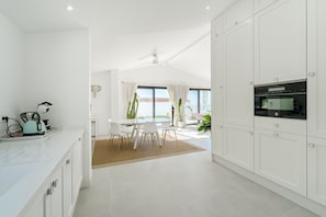 Eine moderne Küche mit weißen Schränken, ein Essbereich mit Tisch und Stühlen sowie ein Blick ins Freie.