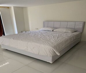 A large bed with a quilted headboard, a bedside table, and a plain wall.