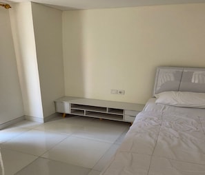 A bedroom with a bed, a white wall, a built-in bench, and a tiled floor.