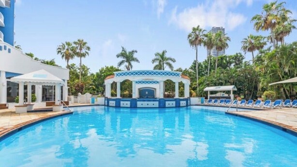 A swimming pool with a pavilion, palm trees, and a building in the background. - 1 bd apartment - Heated Pool, Spa, Walk to the Beach | Broadbeach (Broadbeach)
