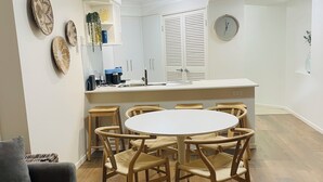 A modern kitchen with white cabinets, a round dining table, and wooden chairs. - 1 bd apartment - Heated Pool, Spa, Walk to the Beach | Broadbeach (Broadbeach)
