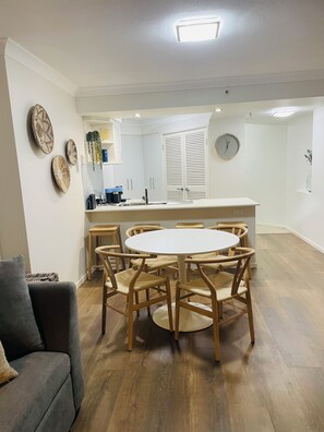 A modern kitchen with white cabinets, a round dining table, and wooden chairs. - 1 bd apartment - Heated Pool, Spa, Walk to the Beach | Broadbeach (Broadbeach)