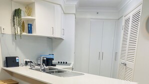 A modern kitchen with a central island, bar stools, white cabinetry, and a built-in oven. - 1 bd apartment - Heated Pool, Spa, Walk to the Beach | Broadbeach (Broadbeach)