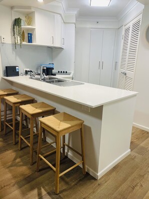 A modern kitchen with a central island, bar stools, white cabinetry, and a built-in oven. - 1 bd apartment - Heated Pool, Spa, Walk to the Beach | Broadbeach (Broadbeach)