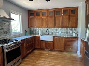 A kitchen with wooden cabinets, a stainless steel stove, and a tiled backsplash. - Ponds Edge - waterfront -King bed -3 bedrooms 2 baths- kayaks - walk to beach (Barnstable)