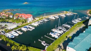 Un port esportiu amb diverses embarcacions amarrades, una zona de pàrquing i edificis amb teulades vermelles.