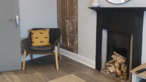 A room with a door, a chair with a cushion, a fireplace with a mirror above it, and a rug on the floor. - Apartment in Belfast City (3) (Belfast)