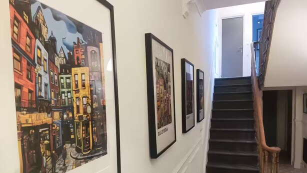 A hallway with framed artwork depicting Dublin, a staircase with a wooden handrail, and a door leading to another room. - Apartment in Belfast City (3) (Belfast)