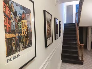 Un couloir orné de tableaux encadrés représentant Dublin, un escalier avec une rampe en bois et une porte donnant sur une autre pièce.