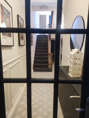 A hallway with framed pictures, a staircase, and a model house. - Apartment in Belfast City (3) (Belfast)
