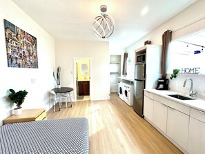 A modern kitchen with a built-in oven, microwave, and sink. There is a dining area with a table and chairs, and a small seating area with a sofa. - Beautiful new 1-bed studio suite with AC & big private yard in charming Burnaby (Burnaby)