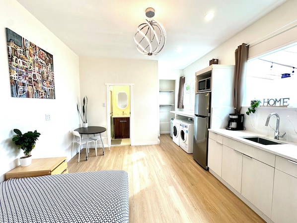 A modern kitchen with a built-in oven, microwave, and sink. There is a dining area with a table and chairs, and a small seating area with a sofa.