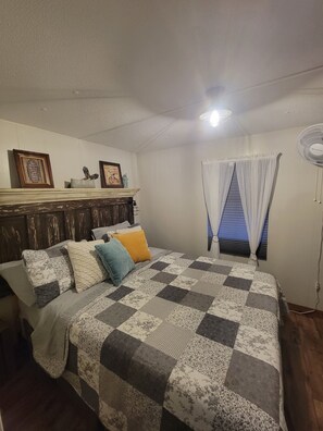 Ein Schlafzimmer mit einem Bett, einem Holz-Kopfteil, einem Fenster mit Vorhängen, einem Wandlüfter und einer Deckenleuchte.