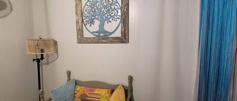 A room with a wooden floor, a sofa with cushions, a framed artwork of a tree, a floor lamp, and a blue curtain.